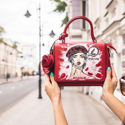 woman-holding-her-red-and-white-leather-handbag-up-high-at-2304764